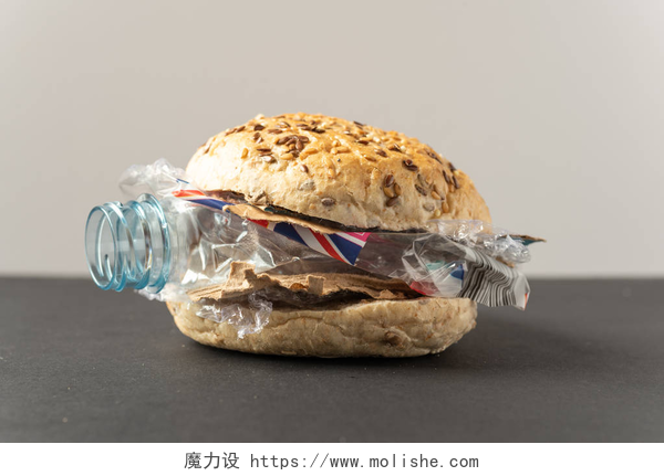 白色背景下黑色桌子上的夹着塑料瓶的面包新鲜美味的汉堡与塑料废料和纸纸板在黑暗的背景。食物概念中的循环再造废物